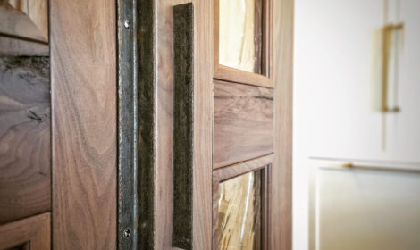 A pair of walnut sliding barn doors mounted to a beautiful kitchen pantry wall. The full glass panels allow light to transfer through into the pantry from the kitchen.
